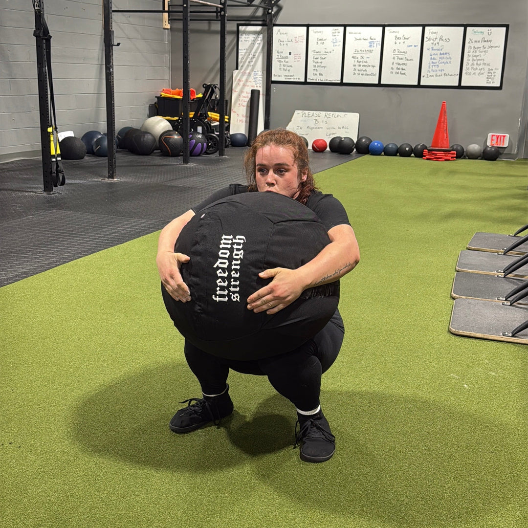person performing a squat with a freedom strength atlas sandbag medicine ball